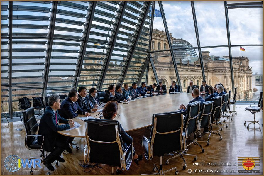 Internationale Delegation an einem großen Konferenztisch unter der Glaskuppel, dahinter das Reichstagsgebäude in Berlin.